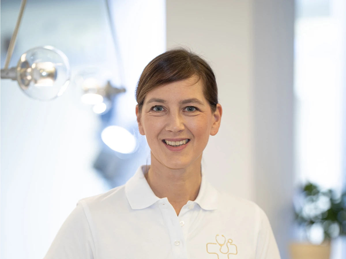 A smiling doctor in a white polo shirt stands in the reception area of the practice. This portrait highlights the team's professional competence and friendliness, ideal for introducing employees and key contacts on the website.