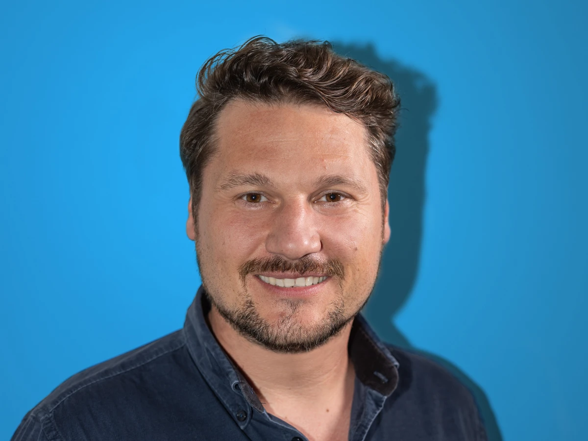 A portrait of a smiling employee in front of a light blue background. This professional portrait photo is ideal for LinkedIn profiles and other business uses.