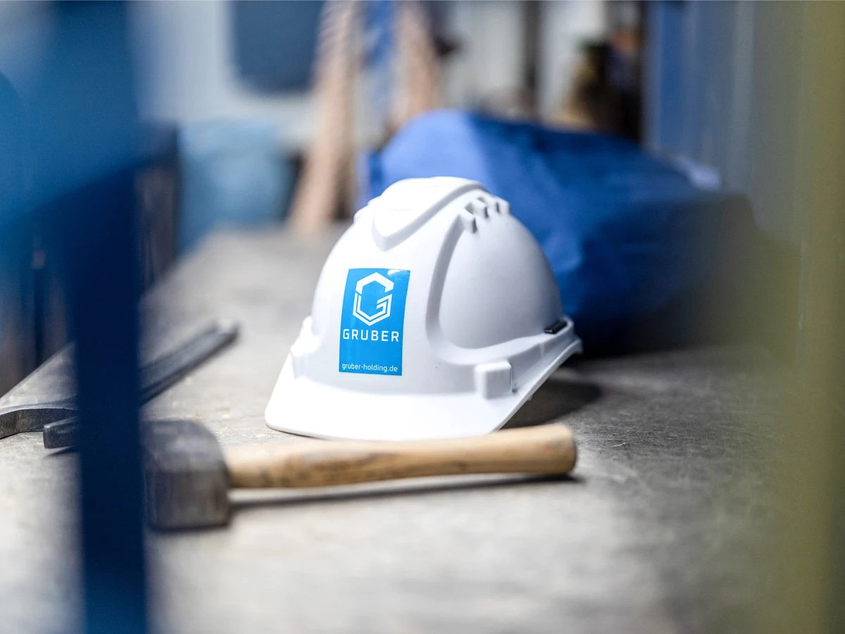 A white construction helmet with the Gruber company logo lies on a worktable. This mood image was created as part of a corporate portrait shoot, showcasing the brand identity in the work environment.